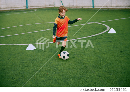 Young boy with soccer ball training at stadium. Football soccer player in motion on green grass sports field. 95155461