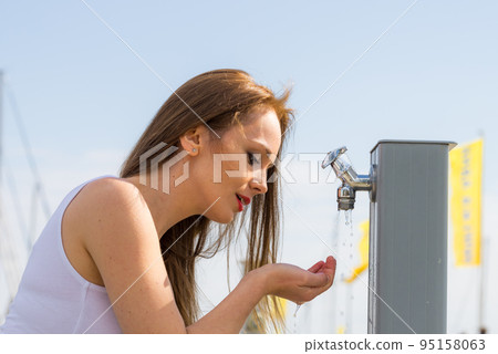 Woman drinking water from street tap Woman drinking water from street tap 95158063