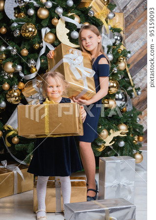 Sisters holding wrapped presents standing beside decorated Christmas Tree on Boxing Day Sisters holding wrapped presents standing beside decorated Christmas Tree on Boxing Day 95159093