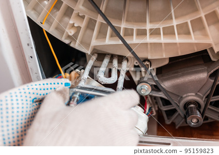 A worker takes out the broken heating element of the washing machine. Hands and spare part close-up. Repair A worker takes out the broken heating element of the washing machine. Hands and spare part close-up. Repair 95159823