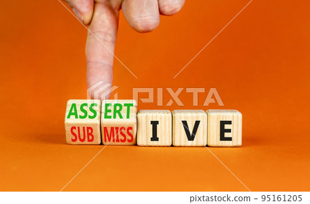 Submissive or assertive symbol. Concept words Submissive and assertive on wooden cubes. Businessman hand. Beautiful orange background. Business, psychological submissive assertive concept. Copy space. Submissive or assertive symbol. Concept words Submissive and assertive on wooden cubes. Businessman hand. Beautiful orange background. Business, psychological submissive assertive concept. Copy space. 95161205