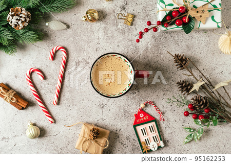 Flat lay of red cup of coffee. Top view of gray background with mug of hot drink, lollipop, gift, fir tree branch, pine cone and Christmas decoration 95162253