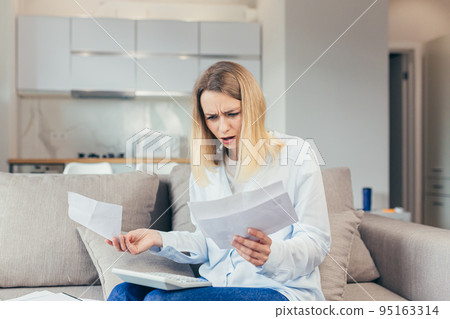 Worried housewife pays inflated bills while sitting on sofa at home, frustrated with work, and monthly income Worried housewife pays inflated bills while sitting on sofa at home, frustrated with work, and monthly income 95163314