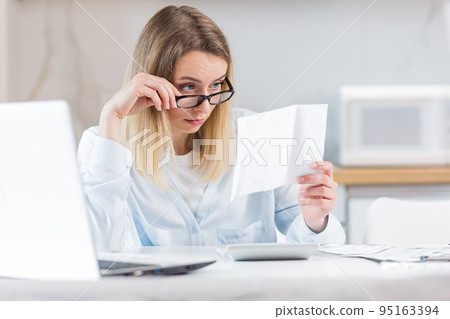 young female housewife sitting a table in house kitchen an incomprehensible deal with paperwork bills and loans. Woman is exhausted and frustrated with documents of enterprise or family budget at home young female housewife sitting a table in house kitchen an incomprehensible deal with paperwork bills and loans. Woman is exhausted and frustrated with documents of enterprise or family budget at home 95163394