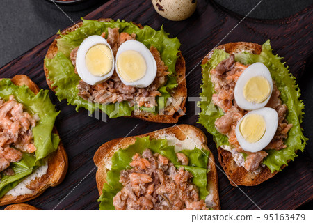 Delicious fresh sandwiches with toast, canned salmon, salad and quail eggs Delicious fresh sandwiches with toast, canned salmon, salad and quail eggs 95163479