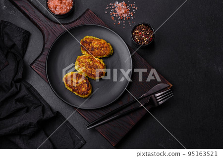 Diet vegetable cutlet from zucchini, carrot, herbs on a black plate Diet vegetable cutlet from zucchini, carrot, herbs on a black plate 95163521