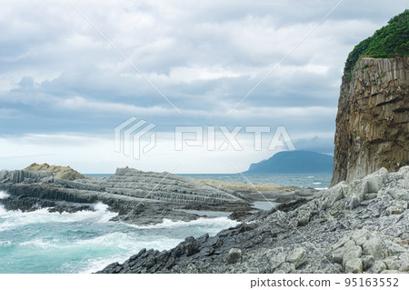 rocky seashore formed by columnar basalt against the backdrop of a stormy sea, coastal landscape of the Kuril Islands 95163552