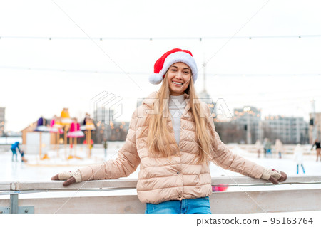 Outdoor portrait young beautiful fashionable woman wearing Santa hat, posing street of European city. Winter Christmas holidays concept. Outdoor portrait young beautiful fashionable woman wearing Santa hat, posing street of European city. Winter Christmas holidays concept. 95163764