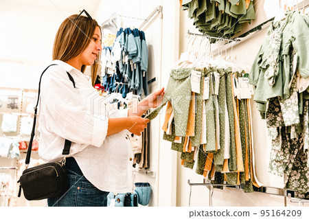 Woman baby clothes shopping. Beautiful pregnant mother buying baby clothes. Pregnant woman hugging shopping child clothes. Everyday baby dress store concept. 95164209