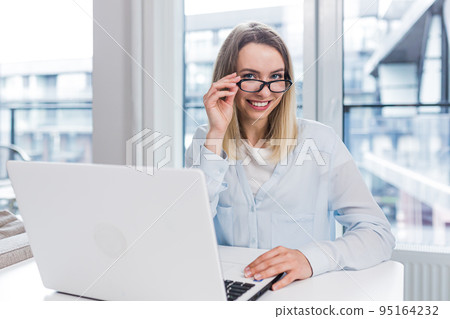 Caucasian happy young freelancer woman sitting at table and talking online on webcam remotely. Female student tells and communicates video call with friends or family indoors. Home or modern office Caucasian happy young freelancer woman sitting at table and talking online on webcam remotely. Female student tells and communicates video call with friends or family indoors. Home or modern office 95164232