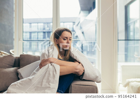 Young woman covered with a blanket sitting on the couch at home sick, feeling bad, bad mood, cold 95164241
