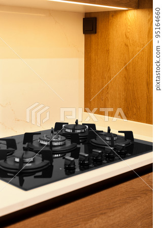 Modern brown wood oak kitchen cabinet equipment, white granite countertops and glass gas stove in a home 95164660