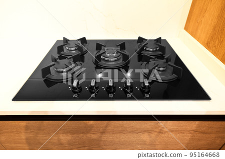 Modern brown wood oak kitchen cabinet equipment, white granite countertops and glass gas stove in a home 95164668