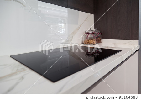 Modern gray white lacquer wood kitchen cabinet and black electric stove on white granite countertop Modern gray white lacquer wood kitchen cabinet and black electric stove on white granite countertop 95164688