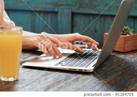 Close Up of Unrecognizable Woman Using Laptop for Her Remote Work While Sitting in Restaurant, Female Freelancer Working Online Through the Internet. Close Up of Unrecognizable Woman Using Laptop for Her Remote Work While Sitting in Restaurant, Female Freelancer Working Online Through the Internet. 95164705