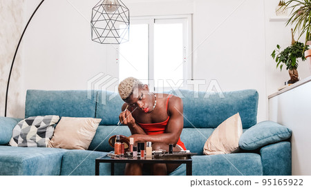 Black african person applying makeup in modern living room at home Black african person applying makeup in modern living room at home 95165922