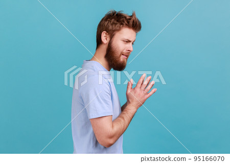 Side view of cunning bearded man schemes something keeps hands together and makes plans, sly expression looking at camera thoughtfully. Indoor studio shot isolated on blue background. Side view of cunning bearded man schemes something keeps hands together and makes plans, sly expression looking at camera thoughtfully. Indoor studio shot isolated on blue background. 95166070