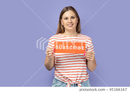 Portrait of winsome adorable pretty woman wearing striped T-shirt holding card with subscribe, female blogger asking to follow her blog. inscription Indoor studio shot isolated on purple background. 95166167