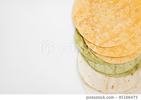 Tomato, spinach flavored and plain wheat tortilla wraps. Spanish or Mexican circular unleavened flatbread from wheat flour. Ingredient for cooking fast food or snack. Top view, white background Tomato, spinach flavored and plain wheat tortilla wraps. Spanish or Mexican circular unleavened flatbread from wheat flour. Ingredient for cooking fast food or snack. Top view, white background 95166473