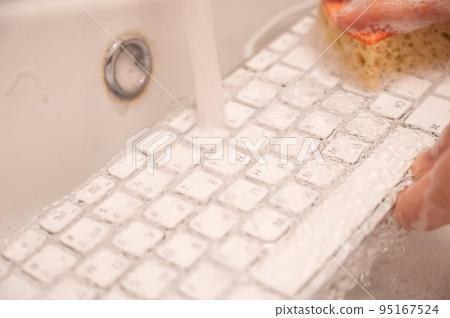 Woman washing white computer keyboard with a sponge with foam. 95167524
