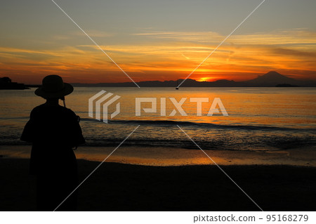 Zushi coast, back view of a woman looking at the sunset on the beach Zushi coast, back view of a woman looking at the sunset on the beach 95168279