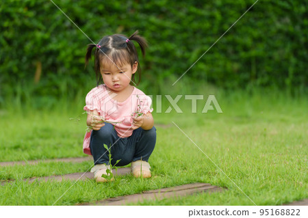 toddler girl sitting and playing grass flower in field 95168822
