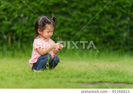 toddler girl sitting and playing grass flower in field toddler girl sitting and playing grass flower in field 95168823