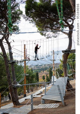 A man is resting in a rope amusement park. Vertical photo. A man is resting in a rope amusement park. Vertical photo. 95169698