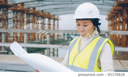 portrait of young Asian forewoman wearing helmet studying blueprint in construction site. People and occupation concept. 95170626