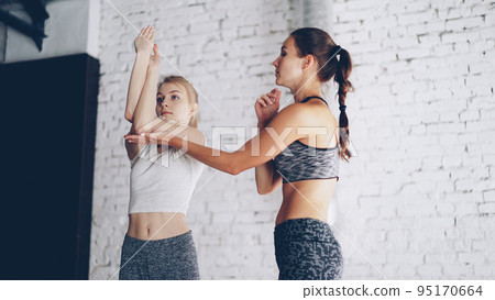 Professional yoga instructor is teaching new student to do arms twists while having individual practice in light wellness studio. Girls are laughing during exercises, relaxing atmosphere. Professional yoga instructor is teaching new student to do arms twists while having individual practice in light wellness studio. Girls are laughing during exercises, relaxing atmosphere. 95170664