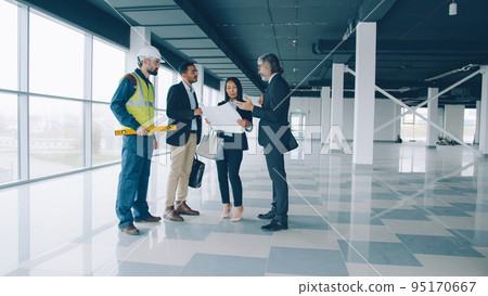 Multi-ethnic group of businesspeople male and female are talking and studying blueprint indoors in modern commercial building. Business and communication concept. 95170667