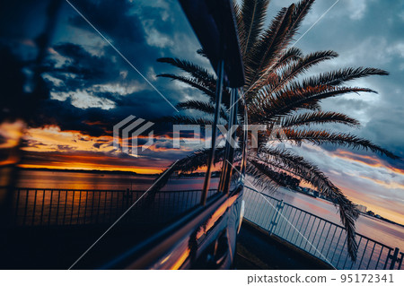 Sunset landscape with palm trees reflected in the car window Sunset landscape with palm trees reflected in the car window 95172341