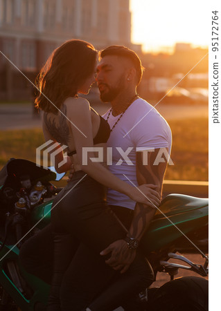 Couple hugging near motorbike at sunset 95172764