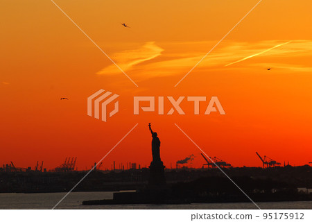 Silhouette of Statue of Liberty and Liberty Island in New York against an orange sunset sky 95175912