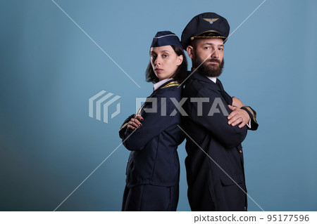 Airplane captain and flight attendant in professional airline uniform standing back to back portrait, studio medium shot. Airliner crew, plane aviator and stewardess, team side view Airplane captain and flight attendant in professional airline uniform standing back to back portrait, studio medium shot. Airliner crew, plane aviator and stewardess, team side view 95177596