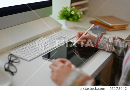 rear view, A hipster female designer in a flannel shirt using tablet at her computer desk. rear view, A hipster female designer in a flannel shirt using tablet at her computer desk. 95178442