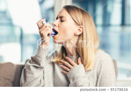 A young woman uses an inhaler for asthma, cough, sick at home 95178616