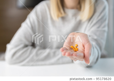 Close-up shot of a woman's hand holding a few yellow pills 95178620