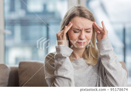 The young woman has a headache, holds her head with her hands and shows pain at home, in the office at work 95178674