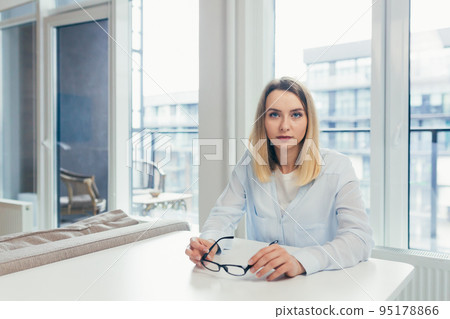 Beautiful young woman with glasses working at home on laptop, online, studying, teaching, making a video call, student, looking at camera, smiling 95178866