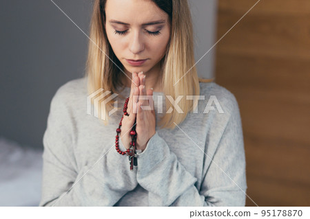 Portrait of a young woman who folded her arms and prayed, holding a rosary in her hands, with her eyes closed, calm 95178870