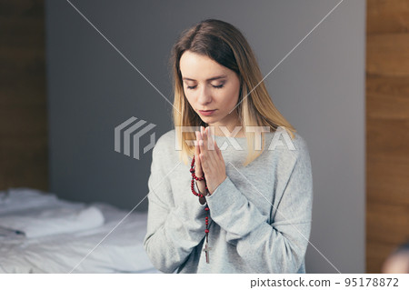 Portrait of a young woman who folded her arms and prayed, holding a rosary in her hands, with her eyes closed, calm Portrait of a young woman who folded her arms and prayed, holding a rosary in her hands, with her eyes closed, calm 95178872