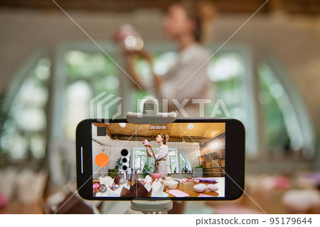 View through phone screen. Young beautiful girl culinary specialist writes video blog on baking. Smiling female vlogger or shooting blog 95179644