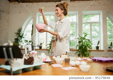 Young charming girl confectioner writes video blog on baking. Smiling female vlogger or shooting blog filming reportage advertising video 95179646