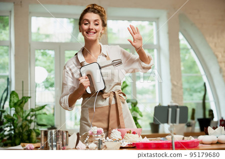 Welcomes subscribers. Young beautiful girl culinary specialist writes video blog on baking. Smiling female vlogger or shooting blog filming reportage advertising video 95179680