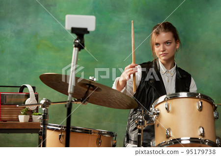 Emotional young girl, rock musician recording music video blog home lesson, playing drums or making broadcast internet tutorial while sitting at record studio 95179738