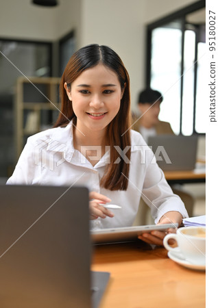Pretty Asian businesswoman looking at her laptop screen while working on her project 95180027