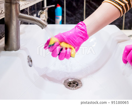 A hand in a pink glove washes a washbasin in the bathroom with a sponge with detergent. 95180065