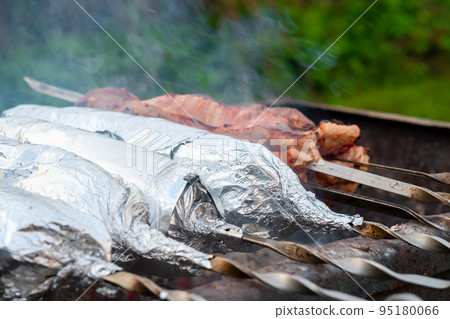 The meat on metal skewers is wrapped in aluminum foil and grilled on charcoal. 95180066