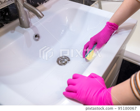 A hand in a pink glove washes a washbasin in the bathroom with a sponge with detergent. 95180067